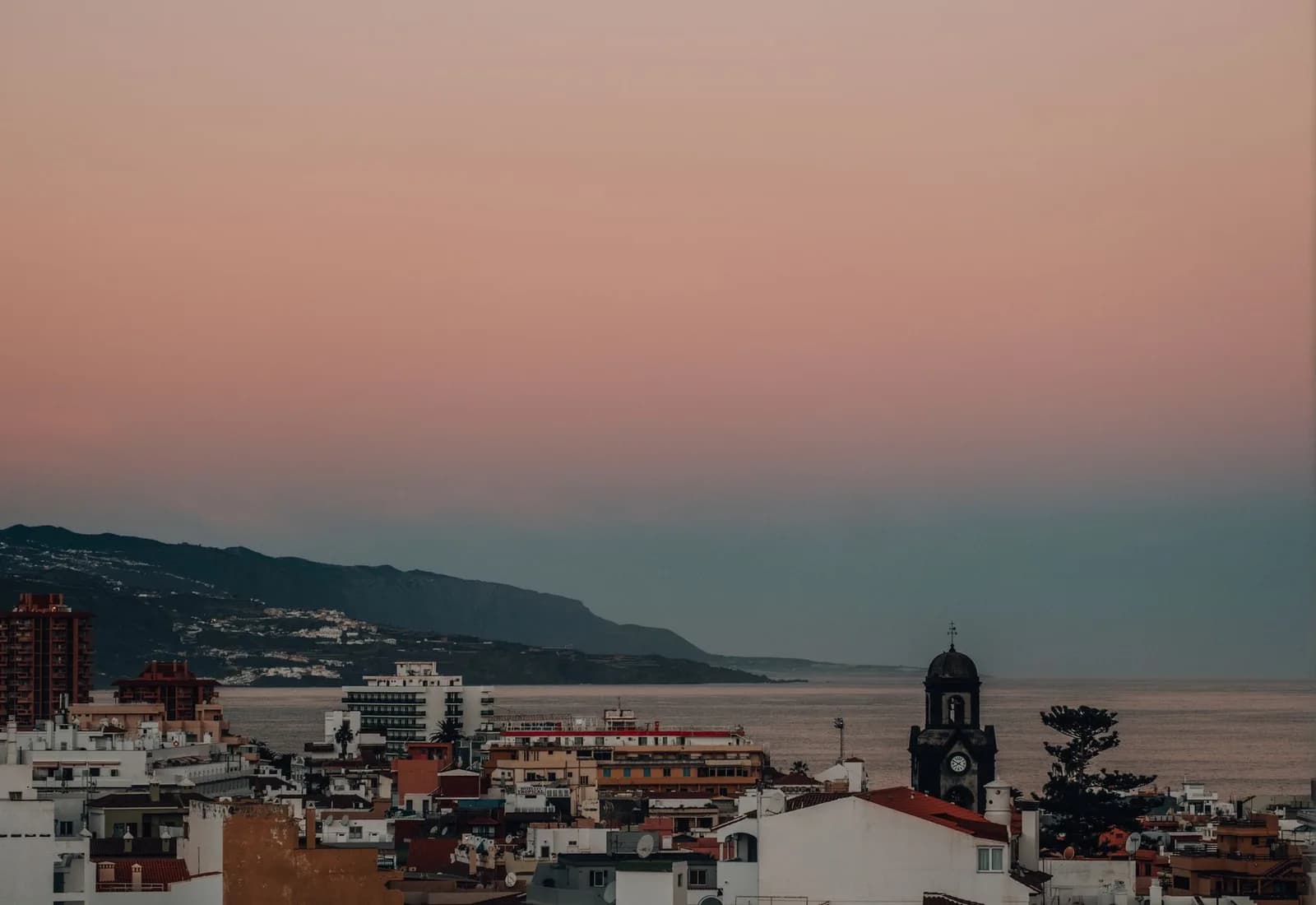 A serene twilight view of a coastal city with an ocean backdrop and pastel skies.